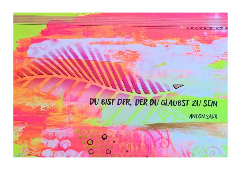 Bunte Graffiti-Wand mit einem großen Blattmuster und dem Schriftzug 'Du bist der, der du glaubst zu sein' von Anton Saur in Schwarz auf einem farbenfrohen Hintergrund aus Orange, Pink, Grün und Blau.